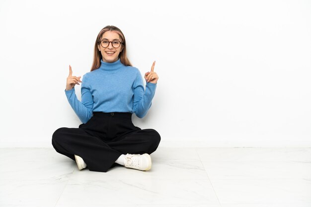 Jonge blanke vrouw zittend op de vloer wijzend op een geweldig idee