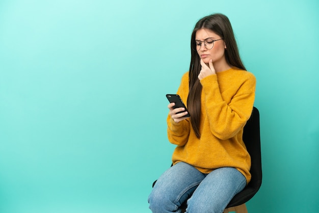 Jonge blanke vrouw zittend op een stoel geïsoleerd denken en een bericht verzenden