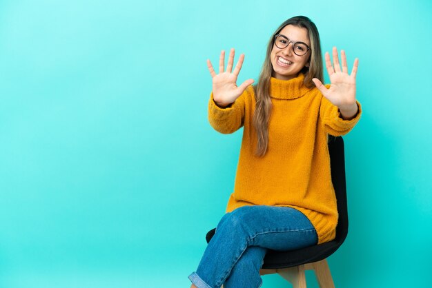 Jonge blanke vrouw zittend op een stoel geïsoleerd op een blauwe achtergrond tien tellen met vingers