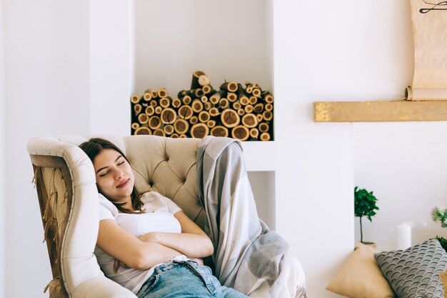 Jonge blanke vrouw zittend op een stoel in de woonkamer slapen na een dag hard werken, een dutje doen of dagdromen