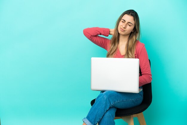 Jonge blanke vrouw zittend op een stoel met haar pc geïsoleerd op blauwe achtergrond met nekpijn