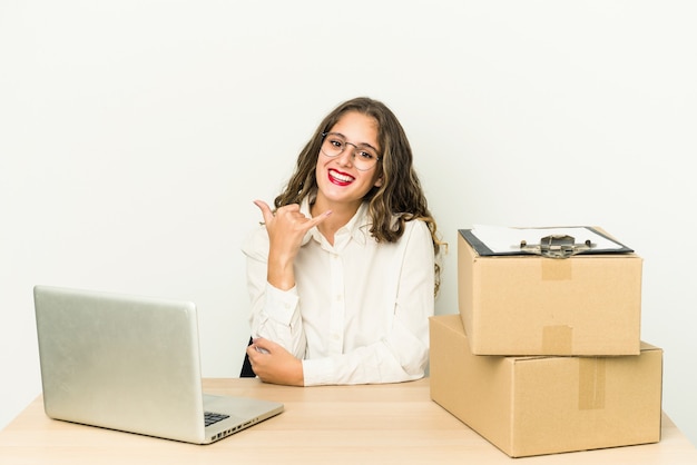 Jonge blanke werknemer van een pakketbedrijf geïsoleerd met een gebaar van het mobiele telefoongesprek met vingers.