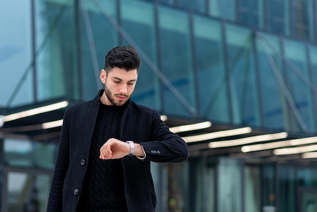 Jonge blanke zakenman die naar zijn horloge kijkt, zakenman die tijd moderne financiële wolkenkrabber op de achtergrond controleert