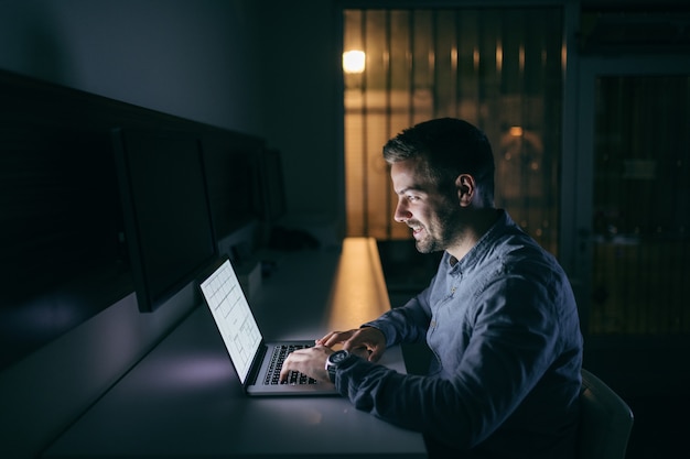 Jonge blanke zakenman typen op laptop zittend in het kantoor 's avonds laat.