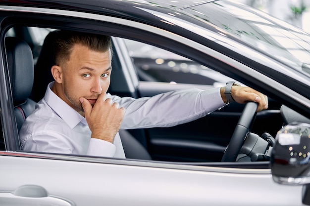 Jonge blanke zakenman zit binnenkant auto achter het stuur