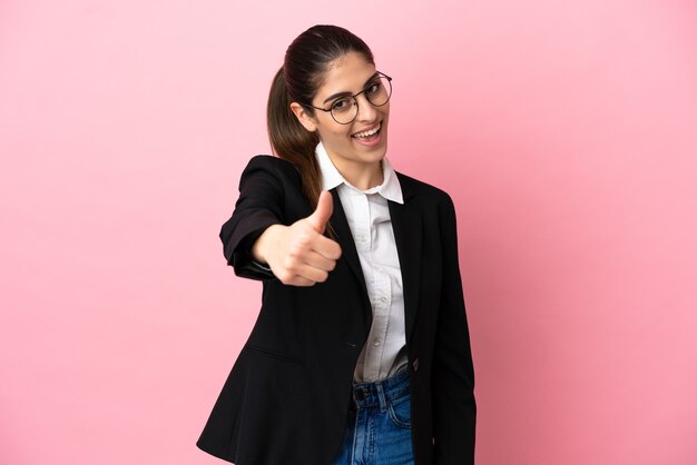 Jonge blanke zakenvrouw geïsoleerd op roze achtergrond met duimen omhoog omdat er iets goeds is gebeurd