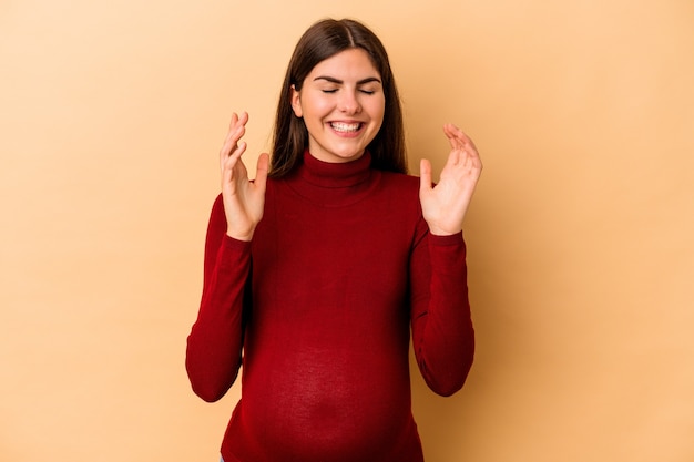 Jonge blanke zwangere vrouw geïsoleerd op een beige achtergrond vrolijk lachen veel. Geluk concept.