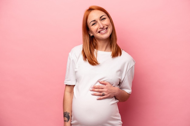 Jonge blanke zwangere vrouw geïsoleerd op roze achtergrond gelukkig, lachend en vrolijk.