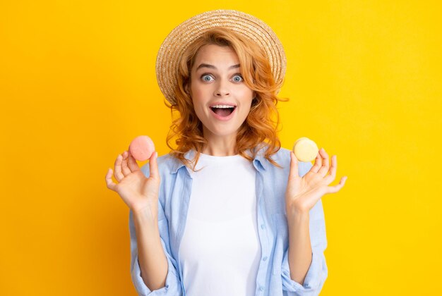 Jonge blije vrouw geïsoleerd op gele achtergrond die bitterkoekjes eet Meisje eet franse macarons