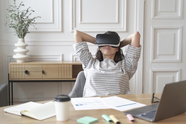 Jonge blije vrouw kantoormedewerker in virtual reality-bril op de werkplek ontspannen in VR-helm op het werk