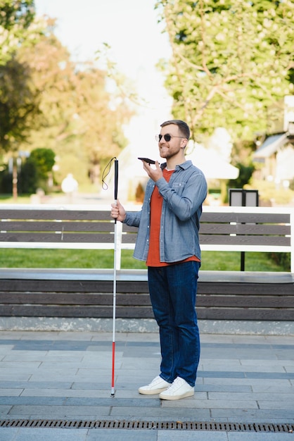 Jonge blinde man met witte wandelstok die over straat loopt in de stad