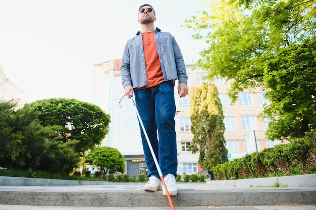 Jonge blinde man met witte wandelstok die over straat loopt in de stad