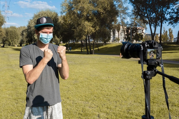 Jonge blogger met een beschermend medisch masker neemt een videoblog op een digitale camera in het park op