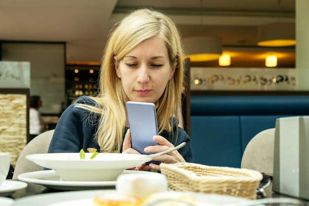 Jonge blonde aan tafel in café maakt foto's van haar eten