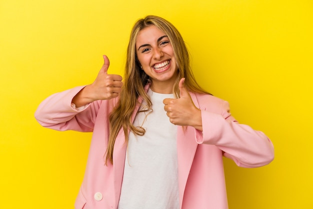 Jonge blonde blanke vrouw die beide duimen opheft, glimlachend en zelfverzekerd.