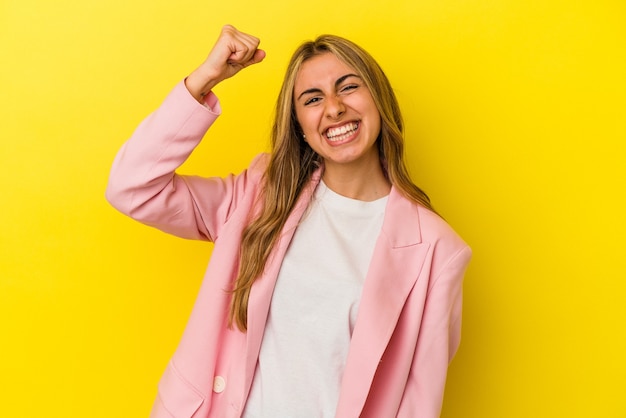 Jonge blonde blanke vrouw die op gele muur wordt geïsoleerd die een overwinning, hartstocht en enthousiasme, gelukkige uitdrukking viert