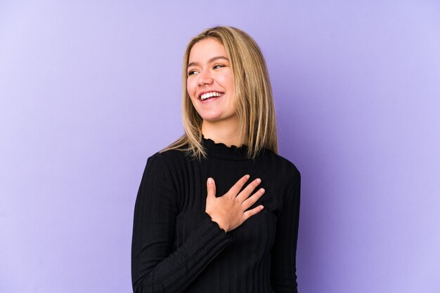 Jonge blonde blanke vrouw geïsoleerd lacht hardop hand op de borst te houden.