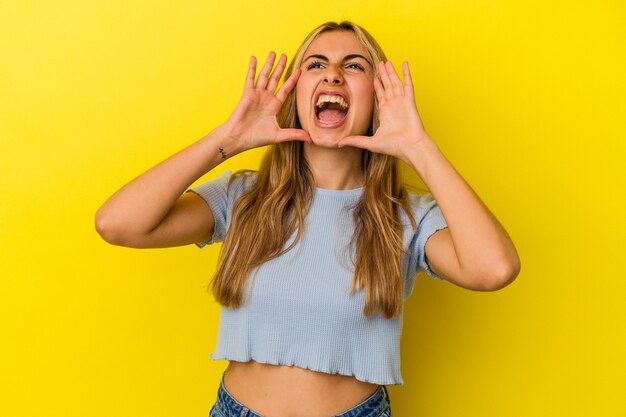 Jonge blonde blanke vrouw geïsoleerd op gele muur opgewonden schreeuwen naar voren.