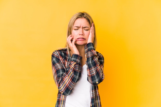 Jonge blonde blanke vrouw geïsoleerd op gele muur troosteloos janken en huilen.