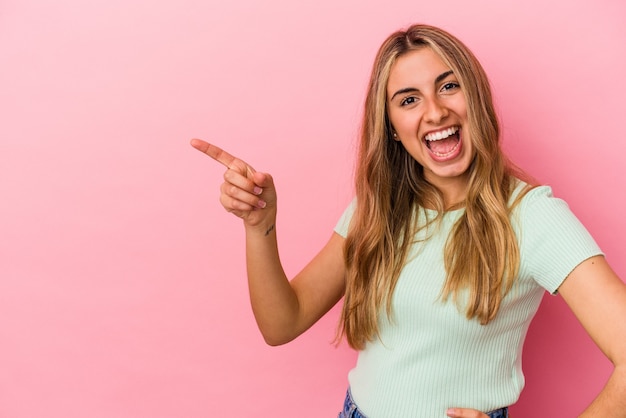 Jonge blonde blanke vrouw geïsoleerd op roze achtergrond glimlachend vrolijk wijzend met wijsvinger weg.