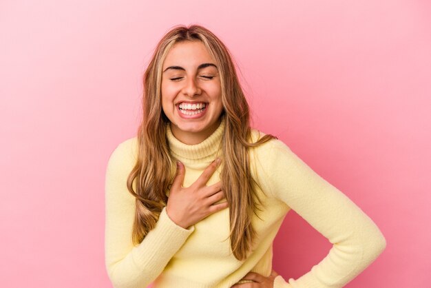 Jonge blonde blanke vrouw geïsoleerd op roze achtergrond lachen houden handen op hart, concept van geluk.