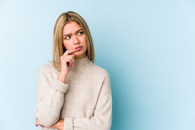 Jonge blonde blanke vrouw geïsoleerd opzij kijkt met een twijfelachtige en sceptische uitdrukking.