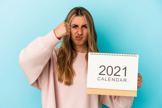 Jonge blonde blanke vrouw holing een kalender geïsoleerd met vuist naar camera, agressieve gezichtsuitdrukking.