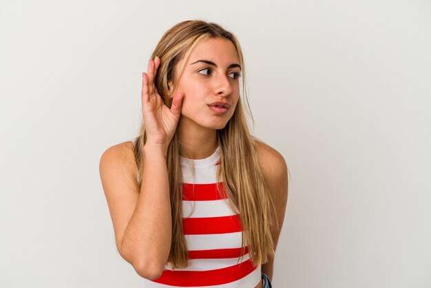 Jonge blonde blanke vrouw op een witte achtergrond geïsoleerd proberen te luisteren naar een roddel.