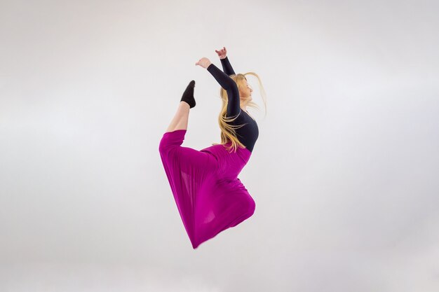 Foto jonge blonde blue-eyed danseres vrouw in lange paarse rok op witte achtergrond