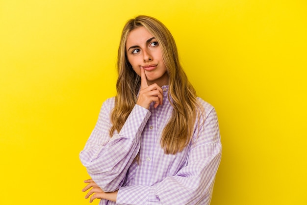 Jonge blonde kaukasische vrouw die op gele muur wordt geïsoleerd die, een strategie plant, nadenkt over de manier van een bedrijf