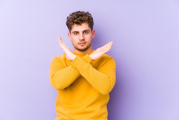 Jonge blonde krullende blanke man geïsoleerd houden twee armen gekruist, ontkenning concept.