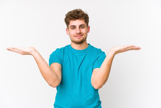 Jonge blonde krullende blanke man geïsoleerd maakt schaal met armen, voelt zich gelukkig en zelfverzekerd.