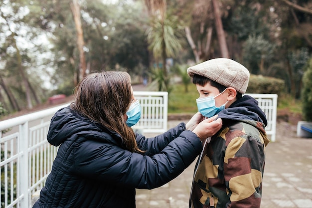 Jonge blonde latijnse moeder met haar jonge zoon die gezichtsmasker in het park gebruikt Eenoudergezin