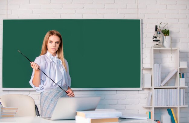 Jonge blonde leraar die op de les wijst schattige jonge vrouw met pointer die bij het bord leert