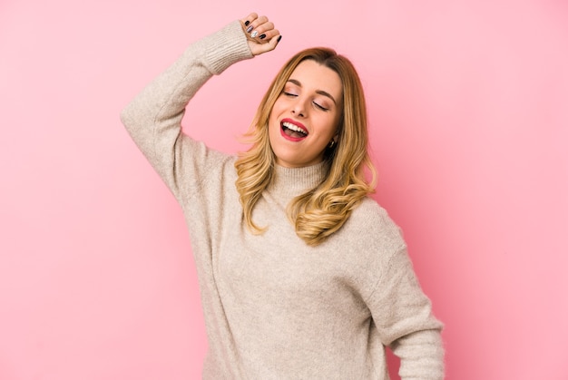 Jonge blonde leuke vrouw die een geïsoleerde sweater draagt die een speciale dag viert, springt en heft wapens op met energie.