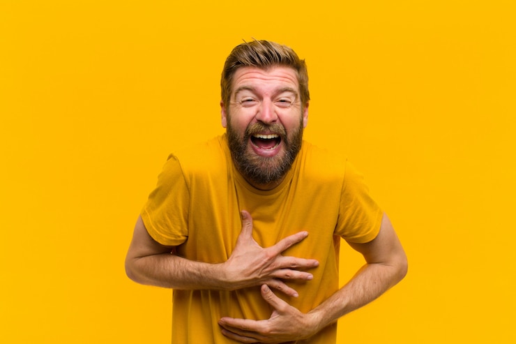Foto jonge blonde man hardop lachen om een hilarische grap, zich gelukkig en vrolijk voelen, plezier maken op oranje muur