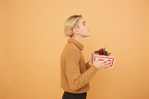 Jonge blonde man houdt een kerstcadeau in zijn handen op de beige achtergrond in de studio