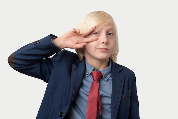 Foto jonge blonde man met blauw jasje en rode stropdas die naar de camera kijkt en een vredesteken toont met vingers geïsoleerd op een witte achtergrond