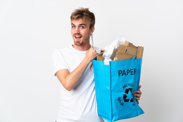 Jonge blonde man met een recycling zak vol papier om te recyclen geïsoleerd op een witte muur een overwinning vieren