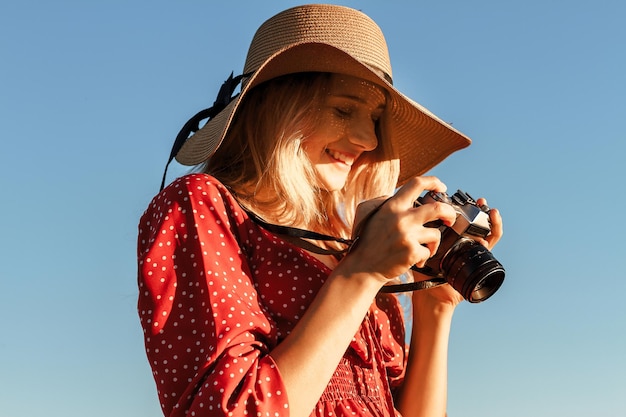 Jonge blonde met een strohoed zit op een hooiberg en maakt foto's met een camera