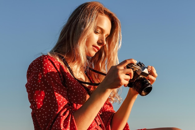 Jonge blonde met een strohoed zit op een hooiberg en maakt foto's met een camera