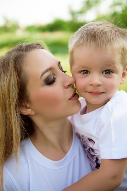 Jonge blonde moeder kust haar zoon en loopt in het park