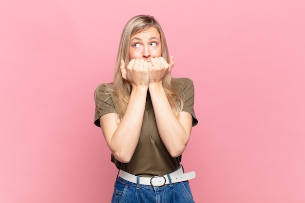 Jonge blonde mooie vrouw die bezorgd, angstig, gestrest en bang kijkt, vingernagels bijt en op zoek is naar zijdelingse kopieerruimte