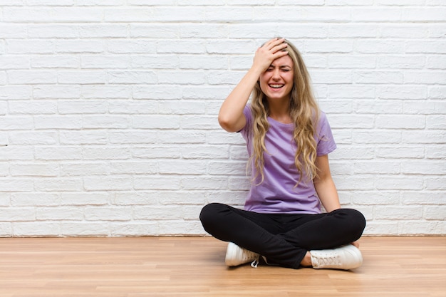 Jonge blonde mooie vrouw die en voorhoofd lachen slaan