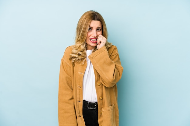 Jonge blonde mooie vrouw geïsoleerd vingernagels bijten, nerveus en erg angstig.