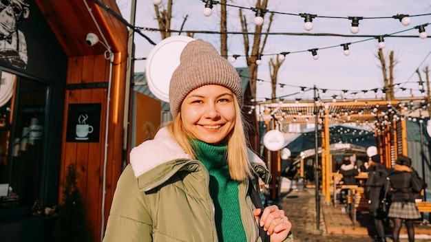 Jonge blonde op de Europese straatvoedselbeurs Ze is blij en lacht op een zonnige winterdag Wazige achtergrond van verschillende straatvoedselverkooppunten