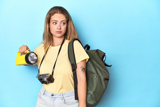 Jonge blonde reiziger met rugzak camera en zaklamp klaar voor een avontuur in een studio