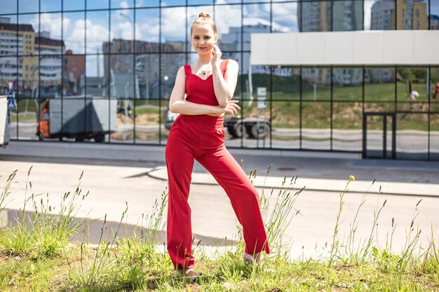 Jonge blonde schoolmeisje in een rood pak en een witte jas poseren op de parkeerplaats