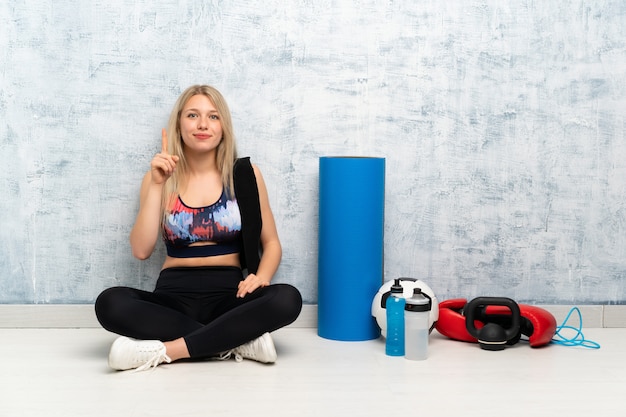 Jonge blonde sport vrouw zittend op het vloer wijzen met de wijsvinger een geweldig idee