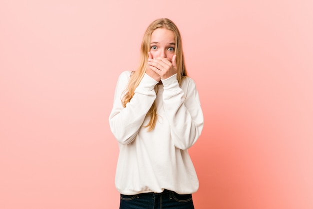 Jonge blonde tienervrouw geschokt behandelend mond met handen